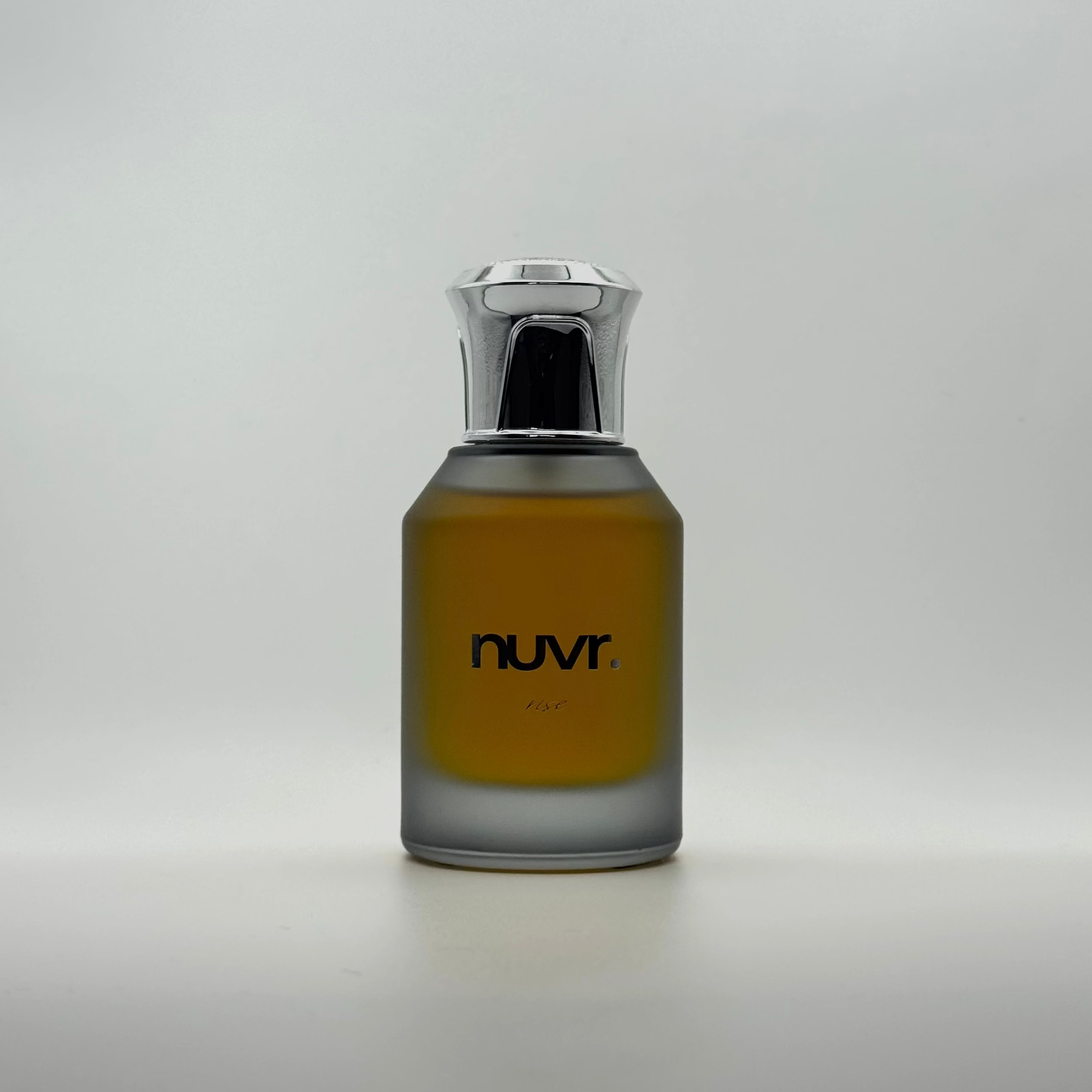 A bottle of nuvr Paris cologne with amber-colored liquid in a frosted glass bottle, featuring a shiny chrome cap, set against a plain light gray background.