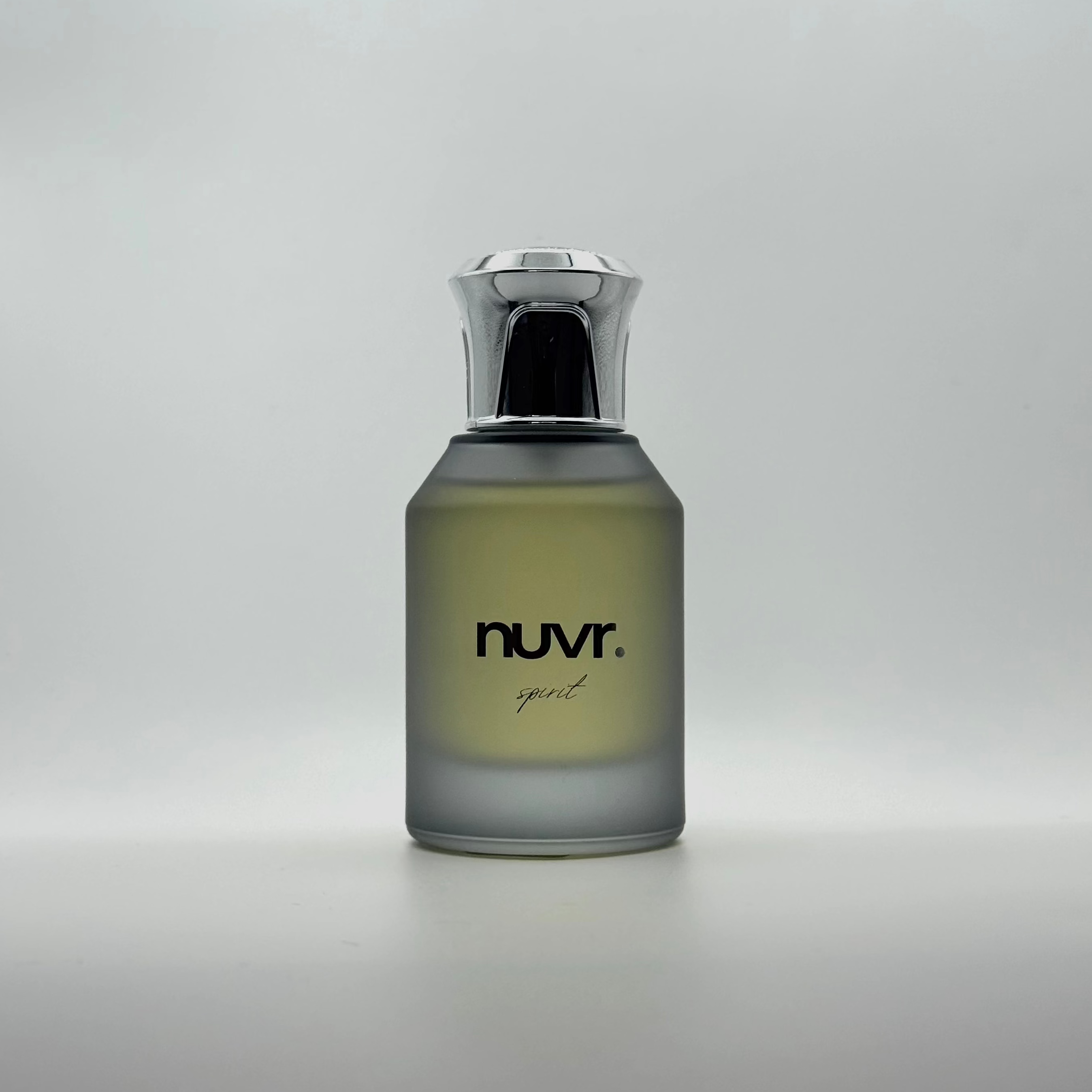 A bottle of nuvr. spirit cologne with a frosted gray glass body, light yellow-green liquid, and a metallic silver cap, set against a neutral gray background.